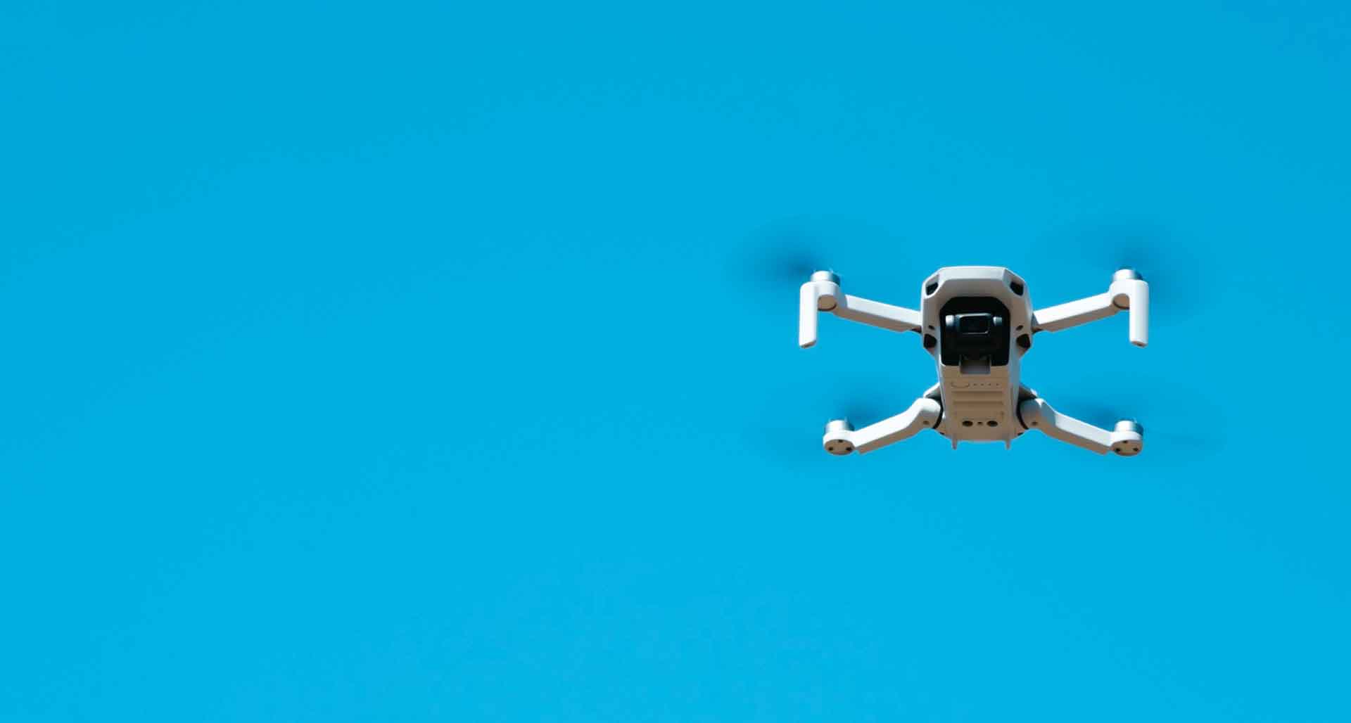 Dron volando sobre fondo azul intenso, para operarlo es fundamental poseer la licencia drones