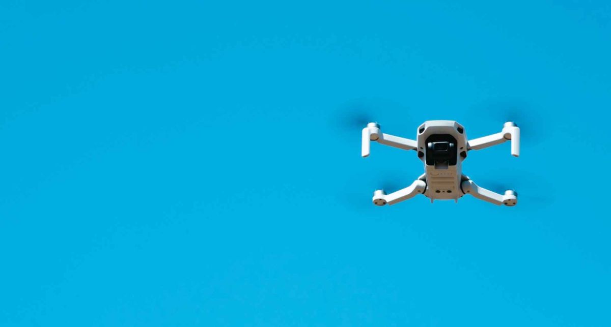 Dron volando sobre fondo azul intenso, para operarlo es fundamental poseer la licencia drones